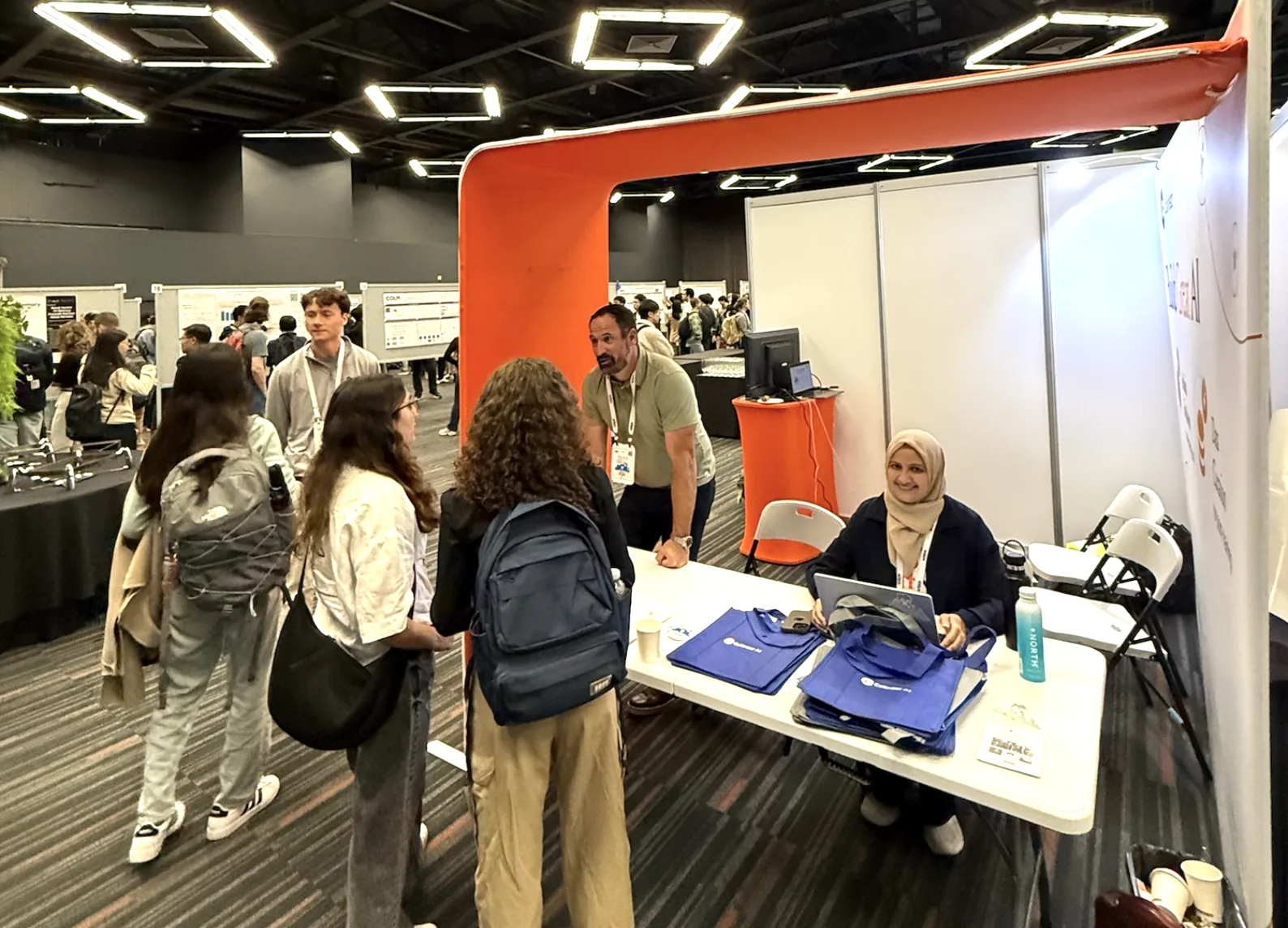 Collinear team members talking with attendees at the Collinear booth at COLM 2025